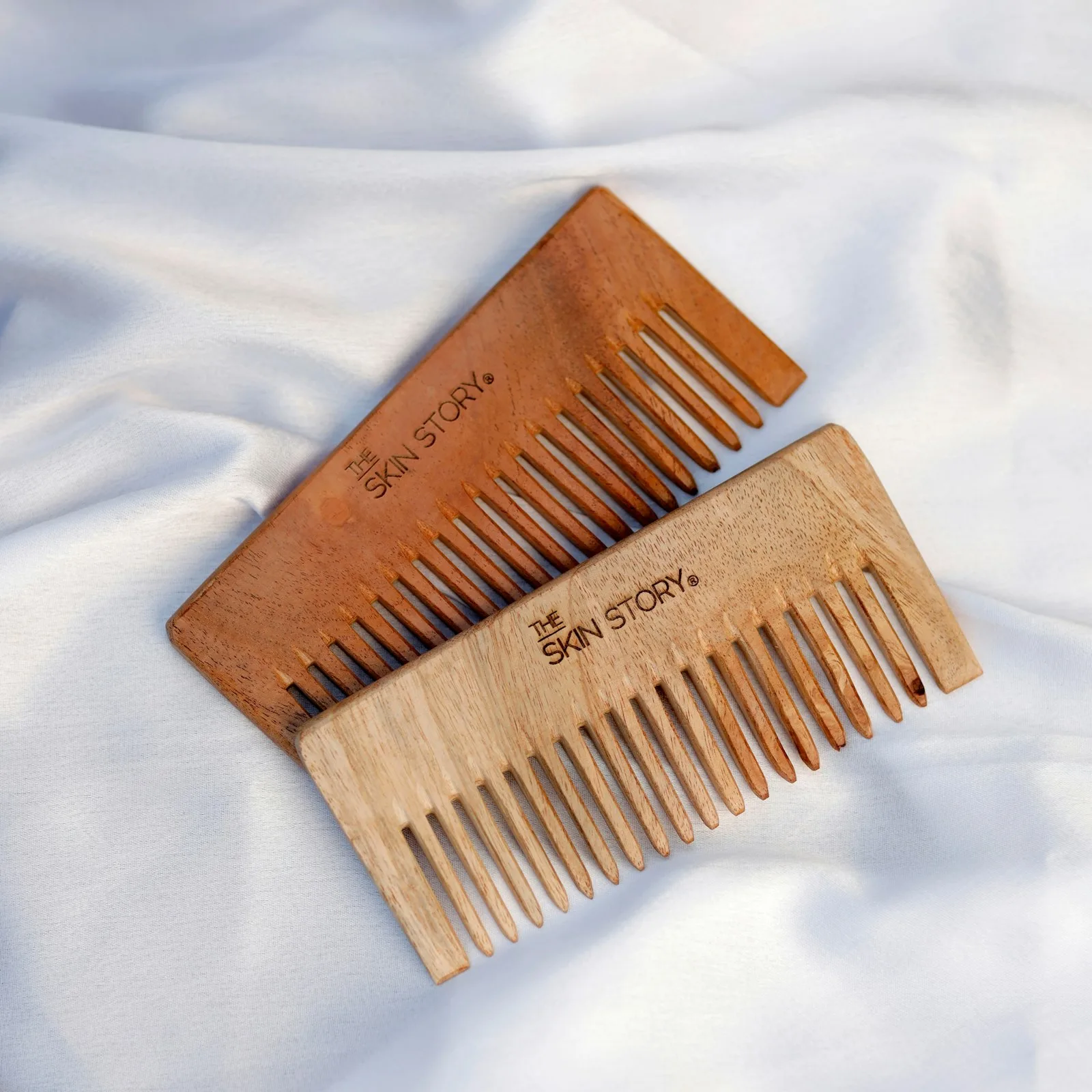 Deux peignes en bois à larges dents posés sur un tissu blanc