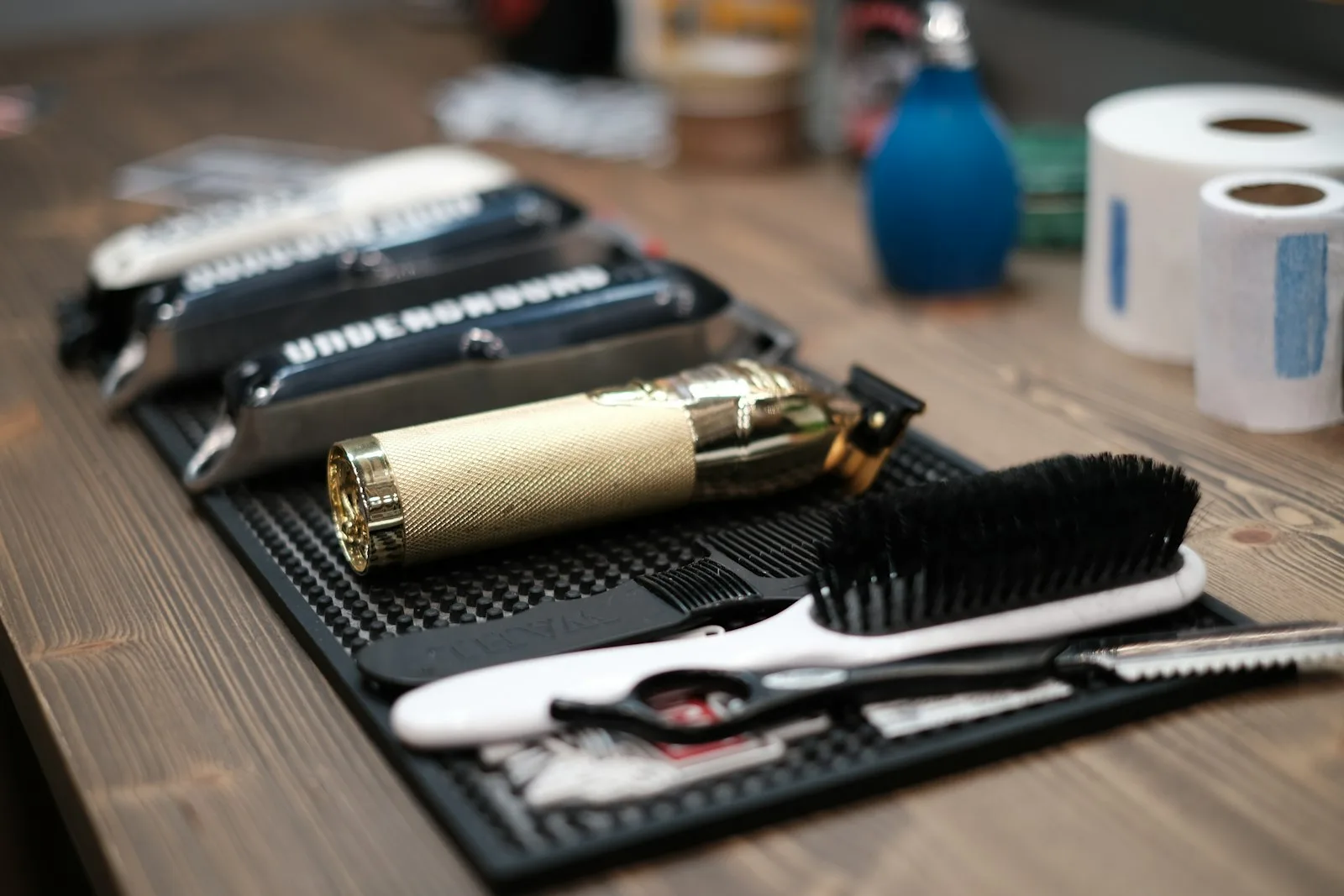 Tondeuse dorée, brosse et ciseaux rangés sur un tapis de travail noir, autres tondeuses en arrière-plan